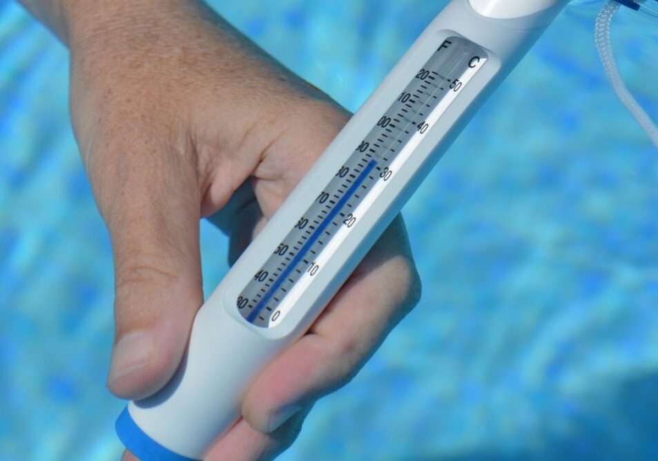 Hand holding a water thermometer, reading the swimming pool temperature at 30 Celsius